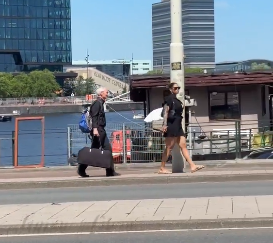 Femeie filmată în timp ce se plimbă și ține în lesă un bărbat cu părul cărunt